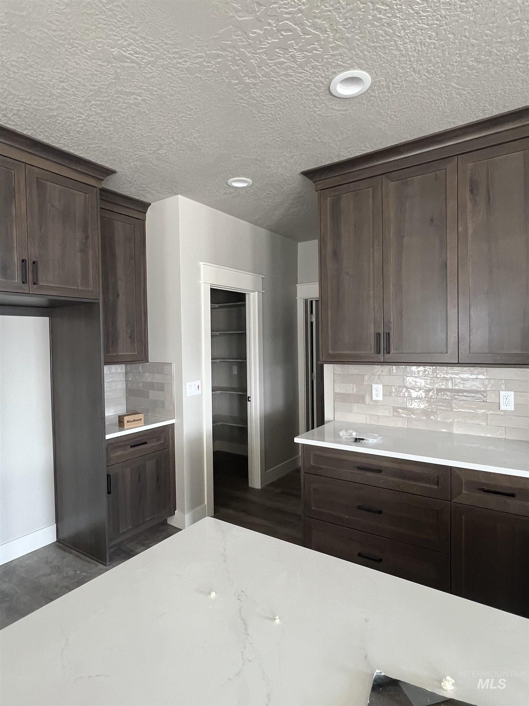 1171 West Recess Way Kuna, ID 83634 - Photo 7 of 15 Kitchen with decorative backsplash, dark wood finish cabinetry, light stone counters, and a textured ceiling
