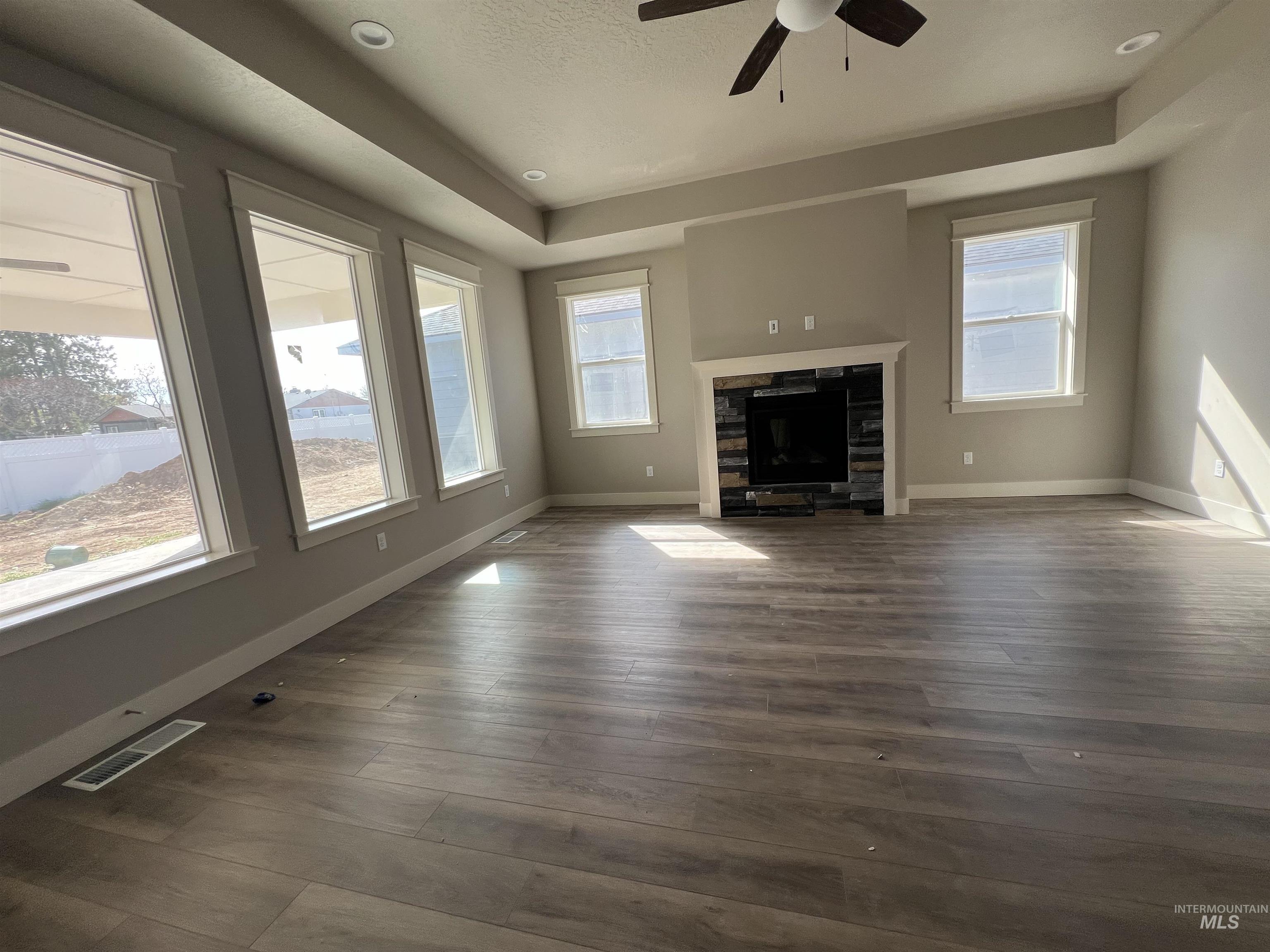 1171 West Recess Way Kuna, ID 83634 - Photo 8 of 15 Unfurnished living room featuring a tray ceiling, ceiling fan, dark wood-style floors, and a glass covered fireplace