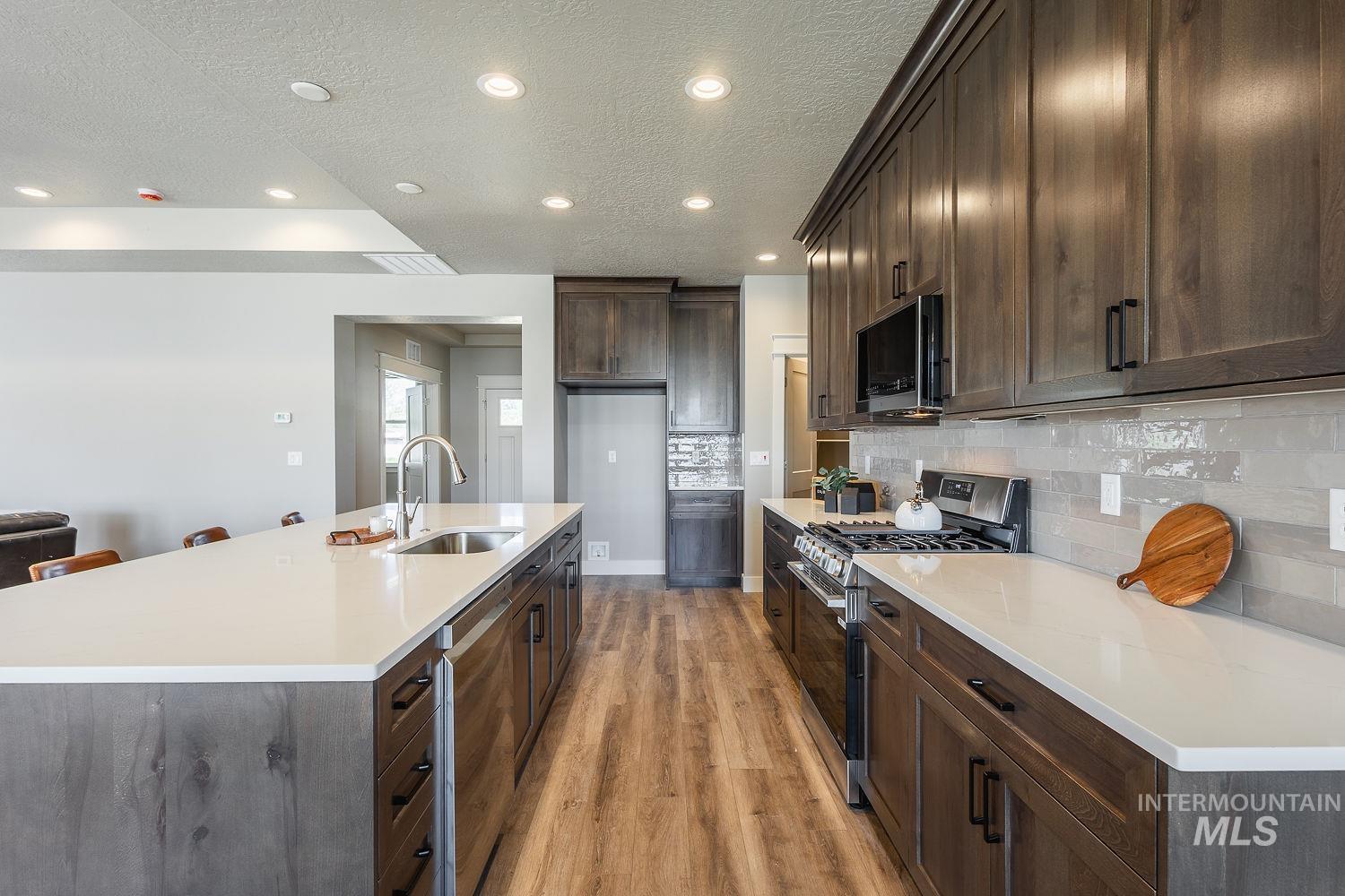 1171 West Recess Way Kuna, ID 83634 - Photo 8 of 28 Kitchen featuring an expansive island with an undermount sink, pendant lighting, wood-finish flooring, dark wood cabinetry with black hardware, and light-toned countertops