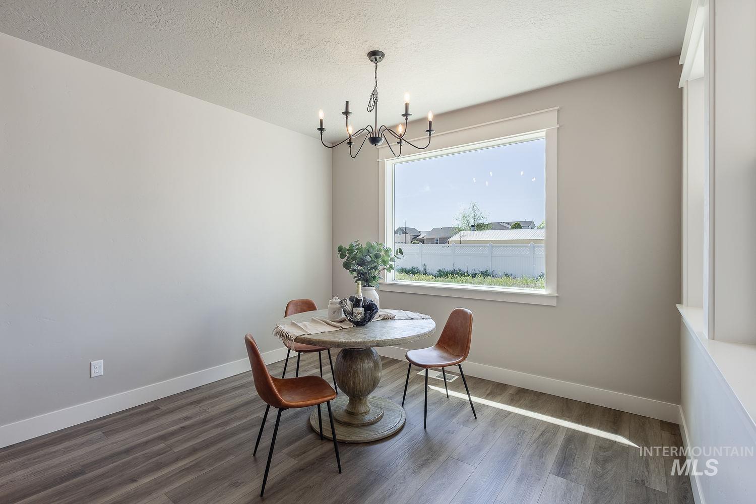 1171 West Recess Way Kuna, ID 83634 - Photo 9 of 28 Dining area featuring wood-finish flooring, a large picture window with white trim, light neutral wall tones, and a black metal chandelier