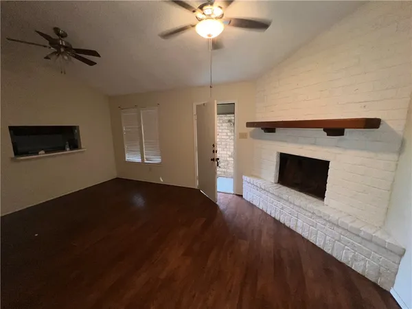 a view of a livingroom with a fireplace a ceiling fan and wooden floor
