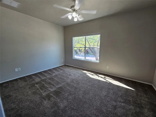 an empty room with a chandelier fan and windows