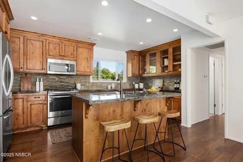 a kitchen with stainless steel appliances granite countertop a refrigerator a sink dishwasher a dining table and chairs with wooden floor