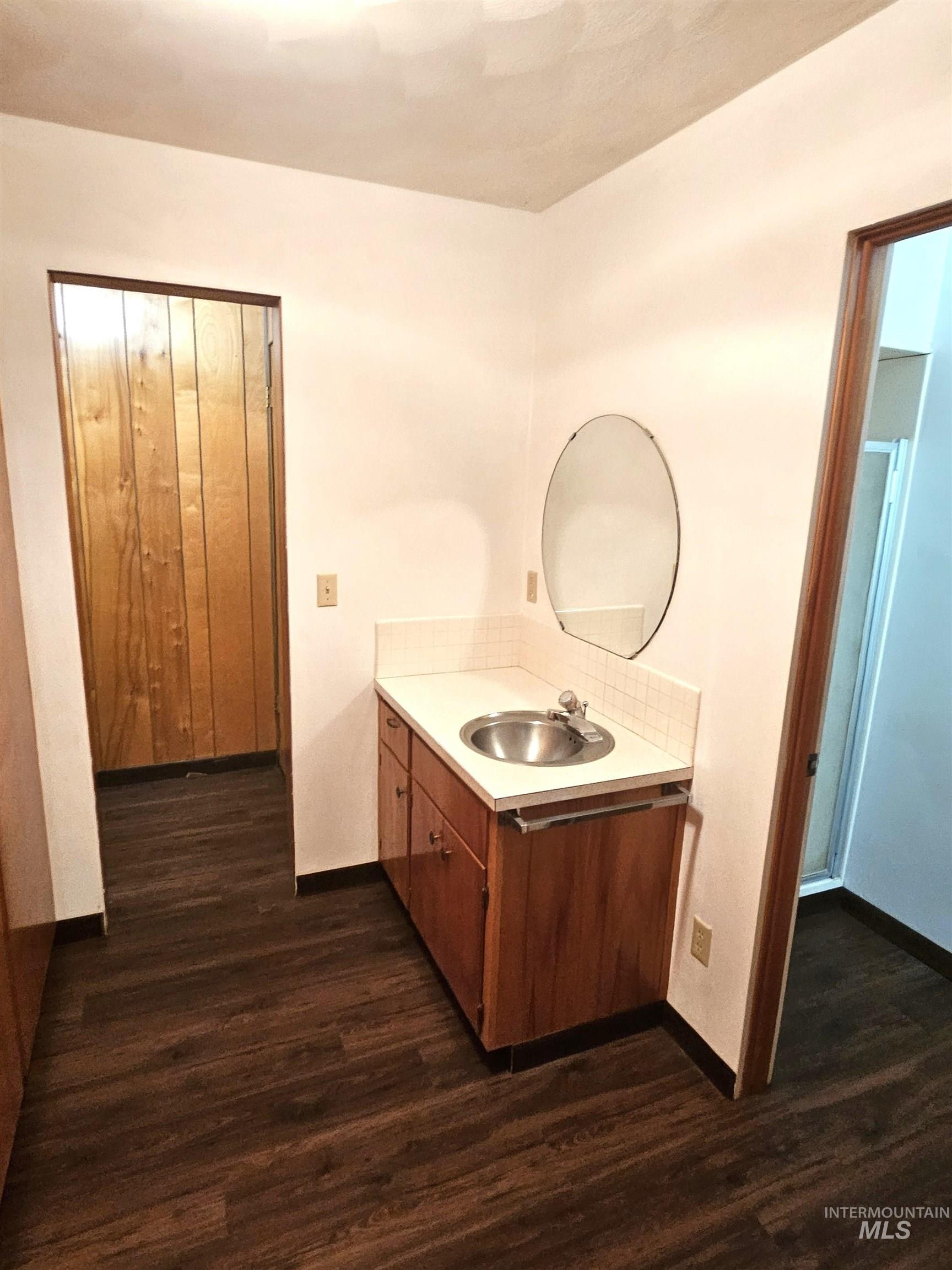 29865 Mission Creek Road Culdesac, ID 83524 - Photo 13 of 43 Vanity area featuring wood-finish cabinetry, a white countertop with an integrated sink, an oval wall mirror, and wood-finish flooring