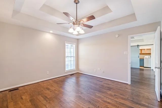 an empty room with wooden floor chandelier fan and windows