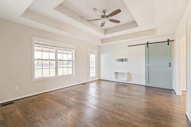 an empty room with wooden floor fan and windows