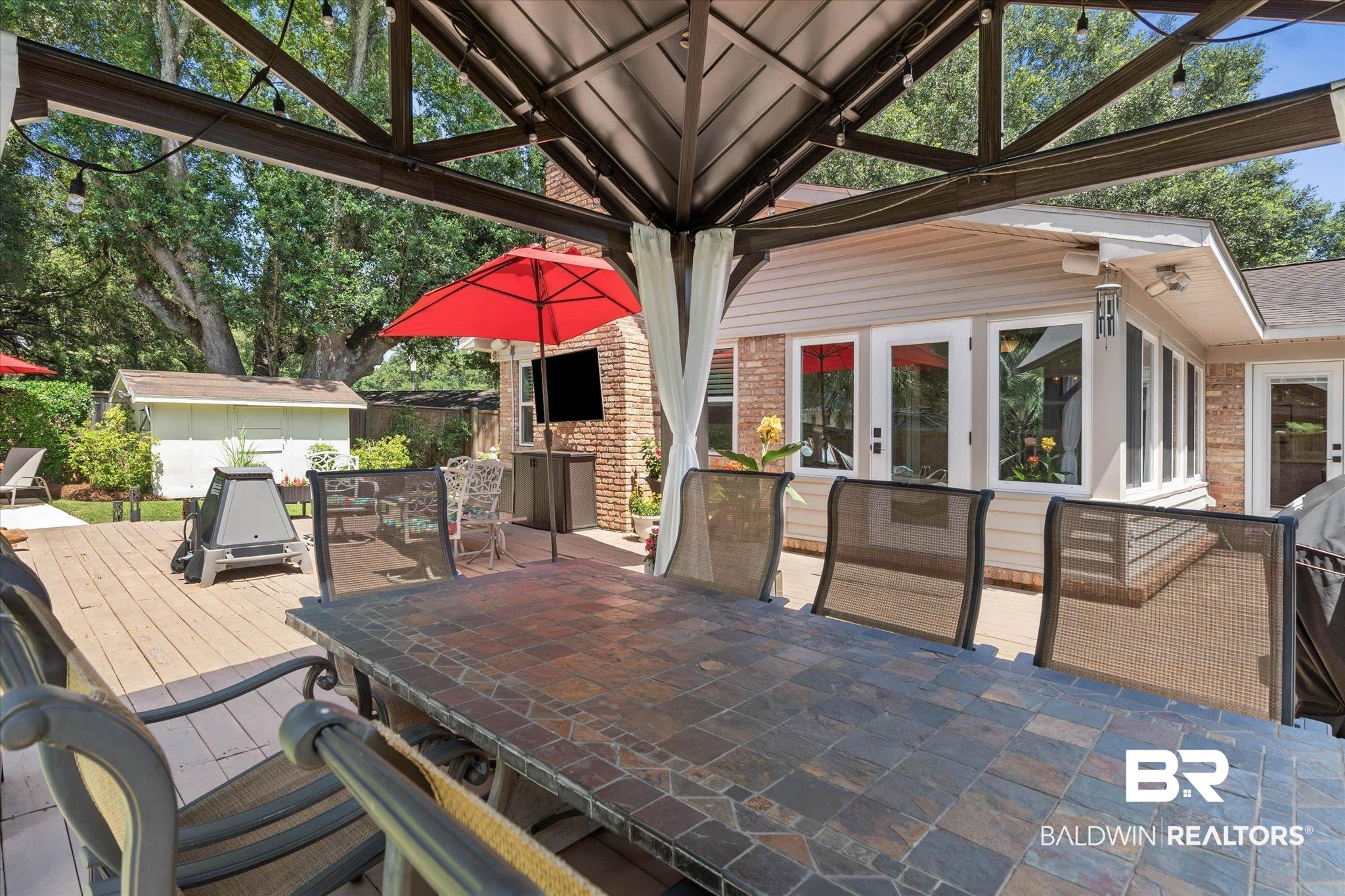 101 Ann Street Daphne, AL 36527 - Photo 24 of 38 Shaded outdoor dining area featuring a tile-top table, integrated string lighting, and a brick-faced outdoor entertainment wall
