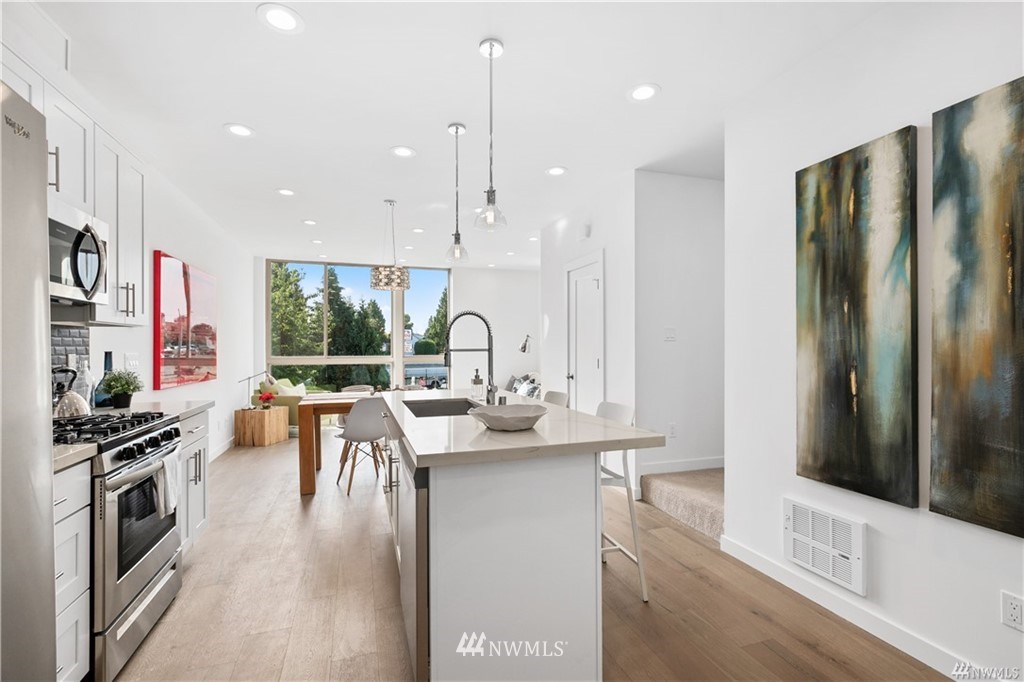 716 North Allen Place Seattle, WA 98103 - Photo 2 of 5 a kitchen with stainless steel appliances kitchen island granite countertop a stove a refrigerator a sink a dining table and chairs with wooden floor