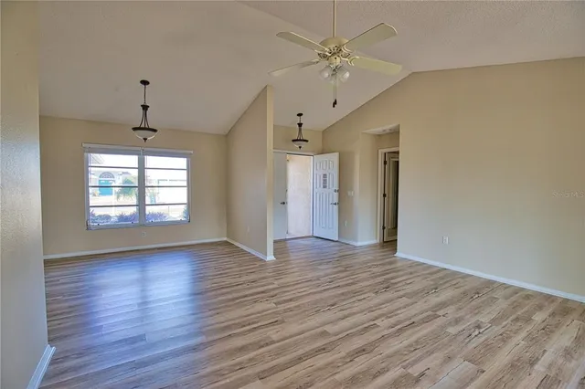 an empty room with wooden floor chandelier fan and windows