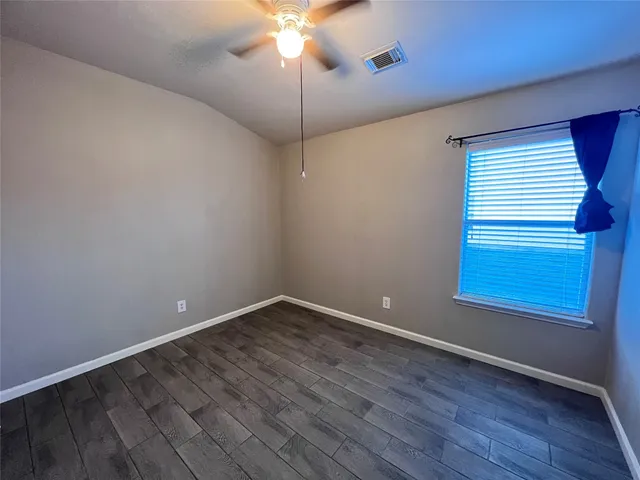 a view of an empty room with wooden floor and a chandelier fan