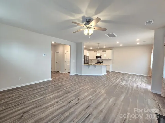a view of an empty room with wooden floor and a kitchen