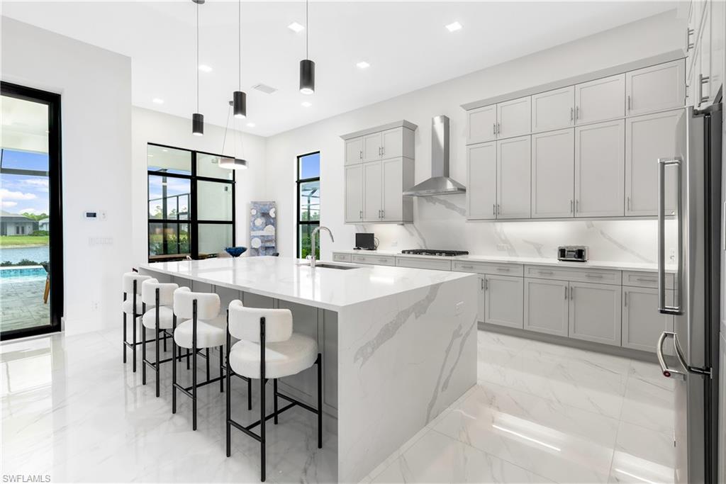 9675 Moonflower Court Naples, FL 34114 - Photo 6 of 32 Kitchen with decorative light fixtures, light stone countertops, an island with sink, light marble finish flooring, and a breakfast bar