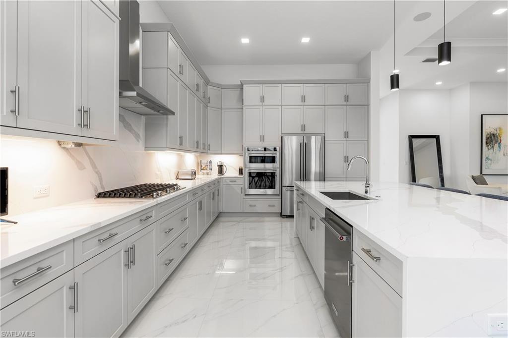 9675 Moonflower Court Naples, FL 34114 - Photo 8 of 32 Kitchen featuring wall chimney range hood, decorative light fixtures, light stone counters, appliances with stainless steel finishes, and a large island with sink