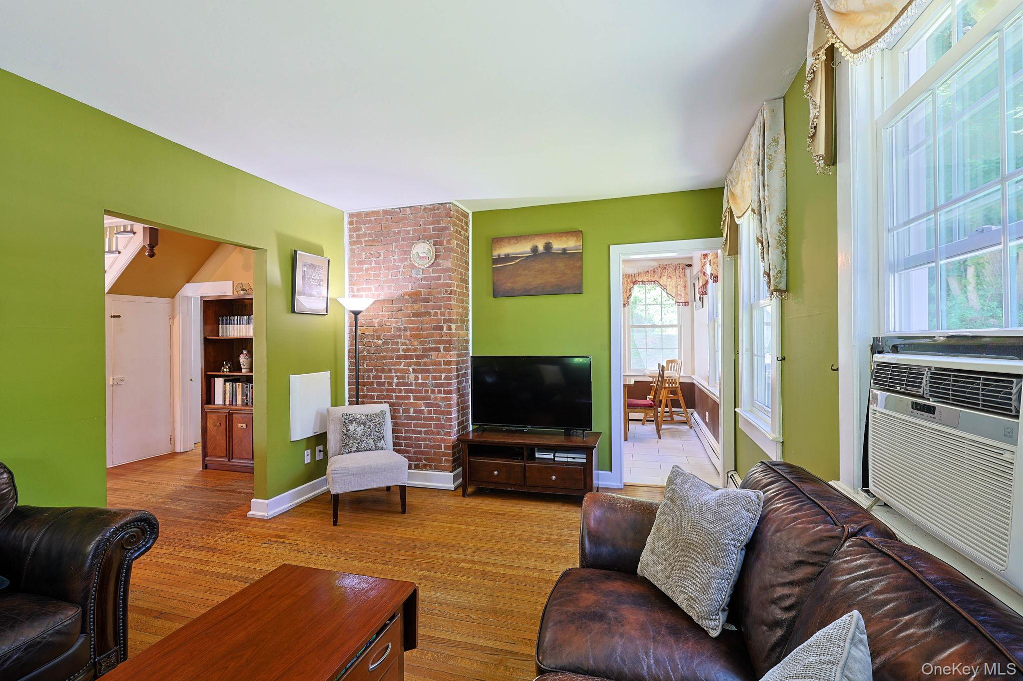 9 Library Road Tuxedo Park, NY 10987 - Photo 6 of 37 Living area featuring wood-finish flooring, exposed brick accent wall, multiple windows, and a built-in window air conditioning unit