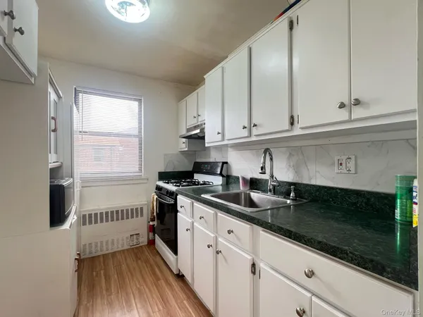 a kitchen with a sink dishwasher a stove and white cabinets with wooden floor