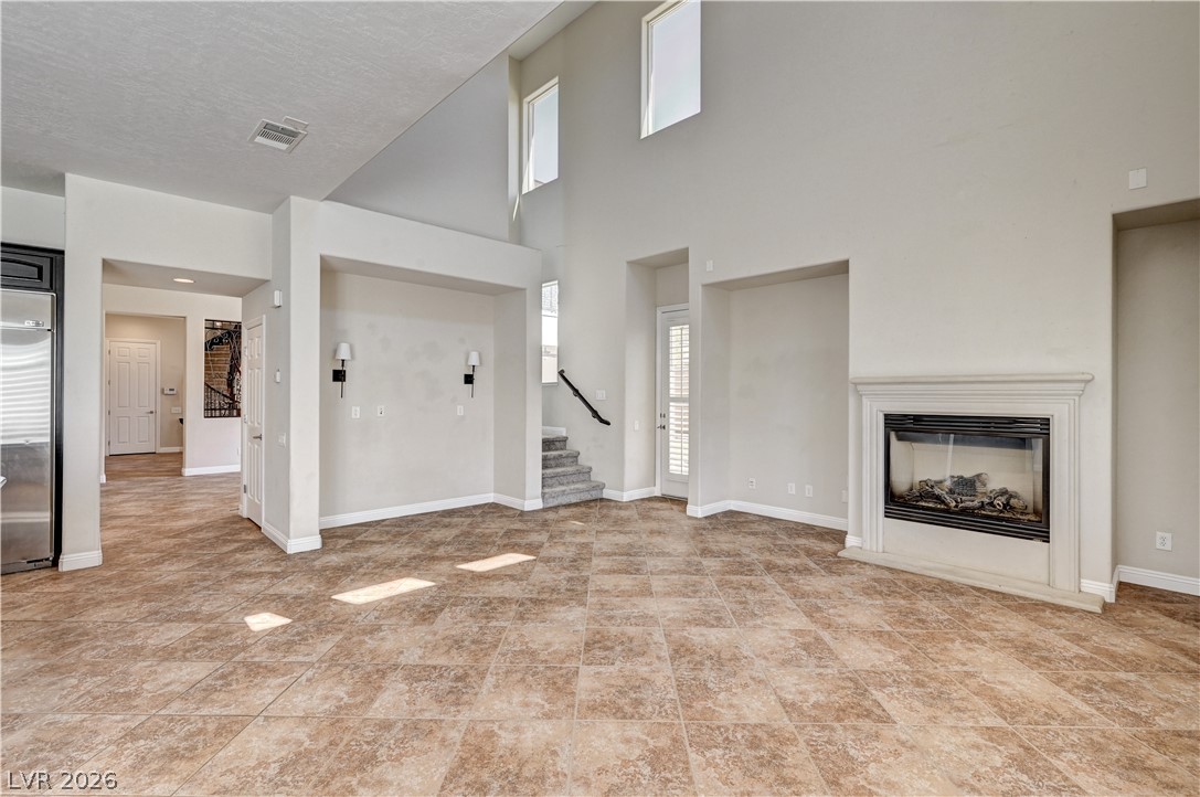 2793 Rosenhearty Drive Henderson, NV 89044 - Photo 13 of 77 A spacious living room featuring soaring ceilings, a cozy fireplace, and natural light illuminating the tiled floors.