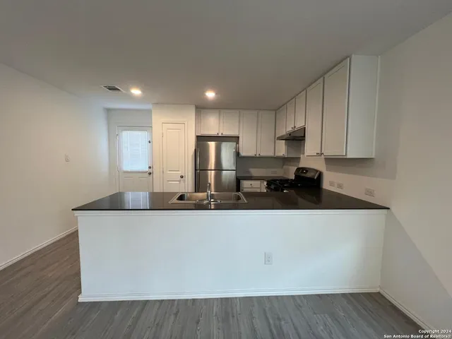 a kitchen with stainless steel appliances granite countertop a sink a stove and a refrigerator with wooden floor