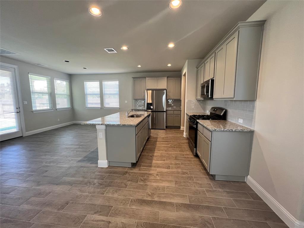 128 Free Stone Drive Georgetown, TX 78628 - Photo 26 of 29 Kitchen featuring an island with a sink and granite countertop, stainless steel appliances, grey cabinetry, and a tile backsplash