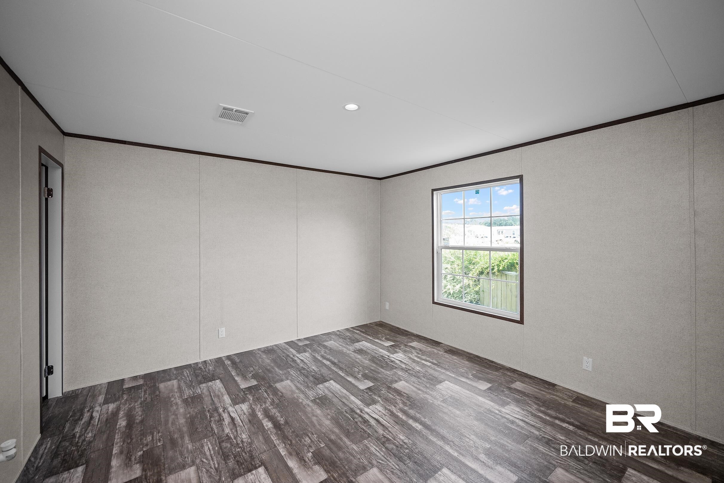 21601 Westside Loop Silverhill, AL 36576 - Photo 36 of 42 Room featuring wood-finish flooring, a double-hung window with dark trim, a recessed ceiling light, a ceiling air vent, and light-toned wall panels