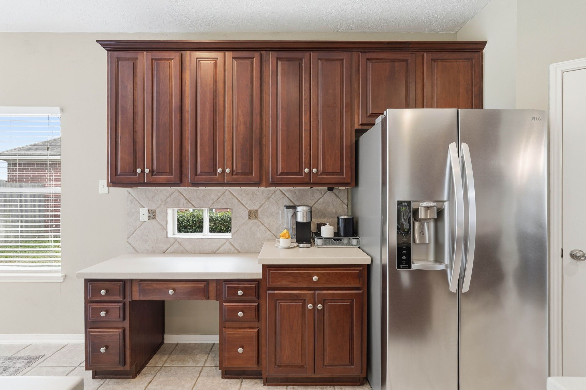 2515 Woodsboro Drive Spring, TX 77388 - Photo 15 of 44 This kitchen features elegant dark wood cabinets, a modern stainless steel refrigerator, and a small built-in desk area. The neutral tile backsplash and countertop provide a clean, classic look, enhanced by natural light.