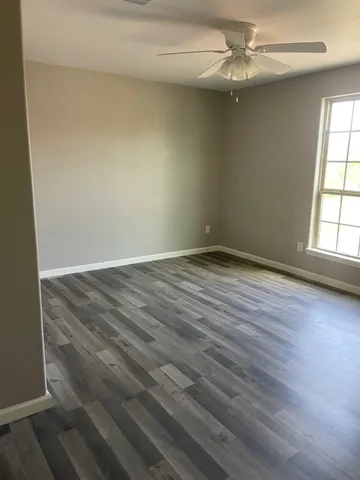 an empty room with wooden floor ceiling fan and windows
