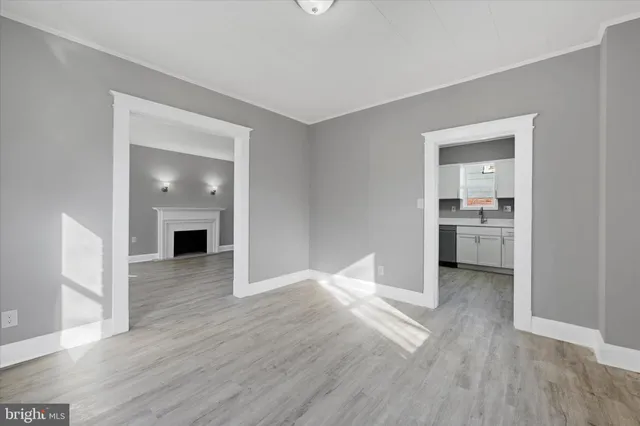 a view of an empty room with wooden floor and a kitchen