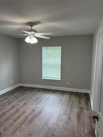 an empty room with wooden floor fan and windows
