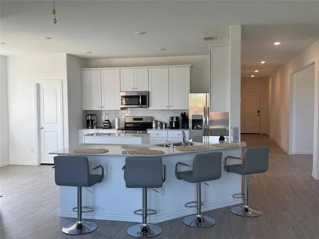 a kitchen with stainless steel appliances kitchen island granite countertop a dining table chairs and a refrigerator