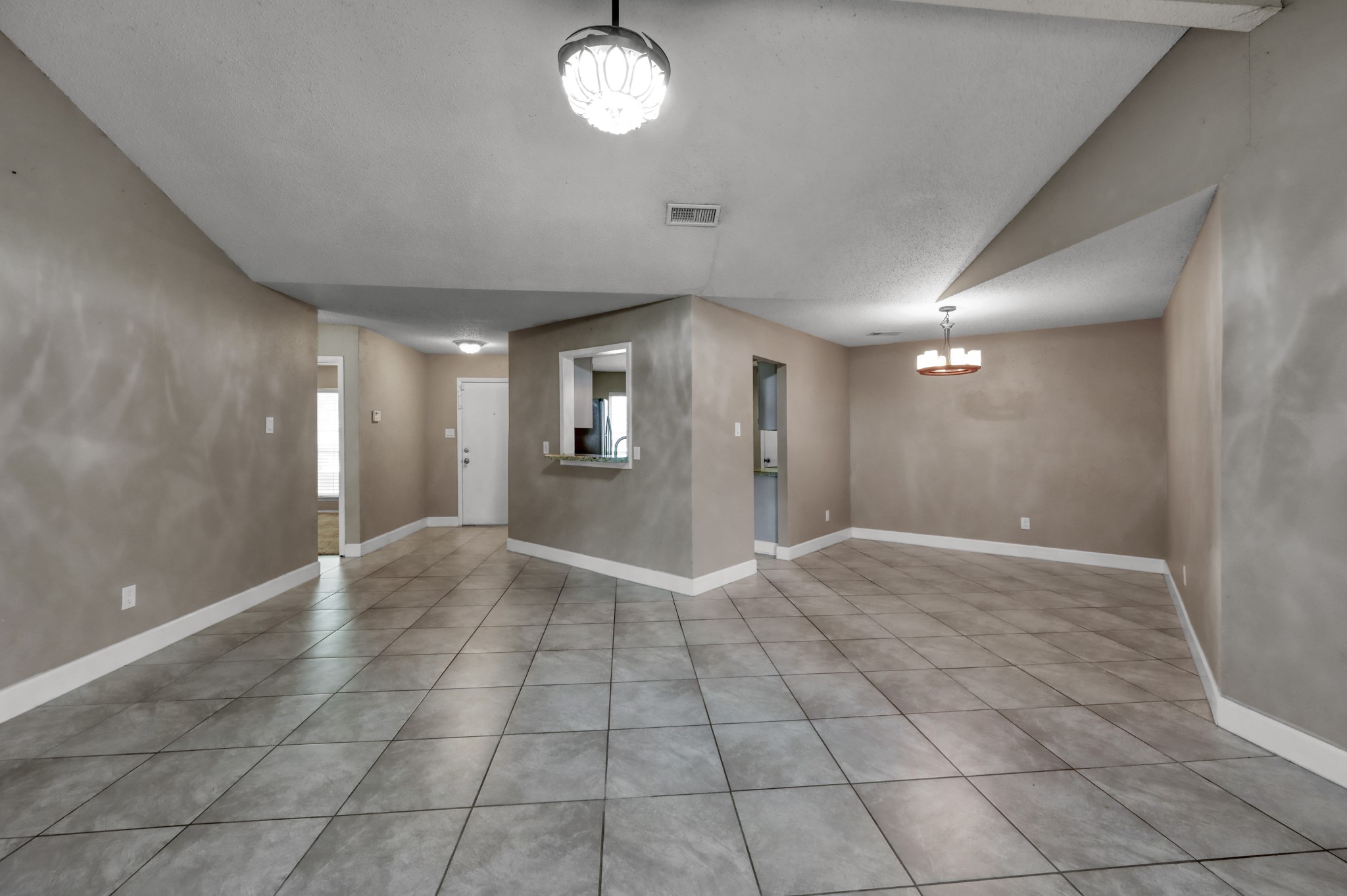 12015 Fallbrook Drive Houston, TX 77065 - Photo 8 of 29 This photo showcases a spacious, open-concept living and dining area with neutral-colored walls and tile flooring. It features two ceiling lights and a pass-through window to the kitchen, creating a versatile space for entertaining and everyday living.