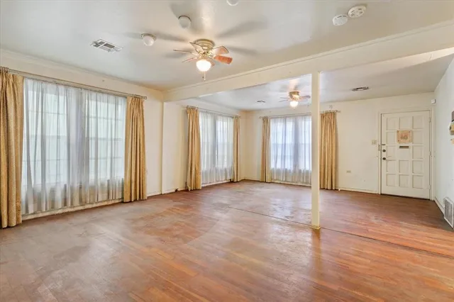 an empty room with chandelier fan and windows