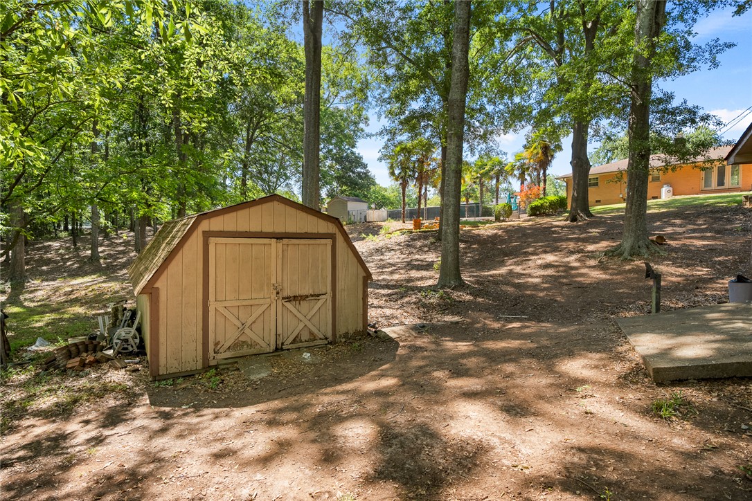 2101 Old Spring Drive Anderson, SC 29625 - Photo 27 of 36 A charming backyard shed provides practical storage amidst a serene, wooded landscape.
