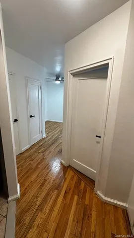 an empty room with wooden floor a ceiling fan and kitchen view