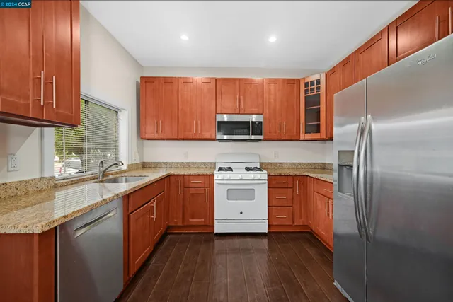 a kitchen with stainless steel appliances granite countertop a refrigerator a sink dishwasher a stove top oven a refrigerator and cabinets with wooden floor