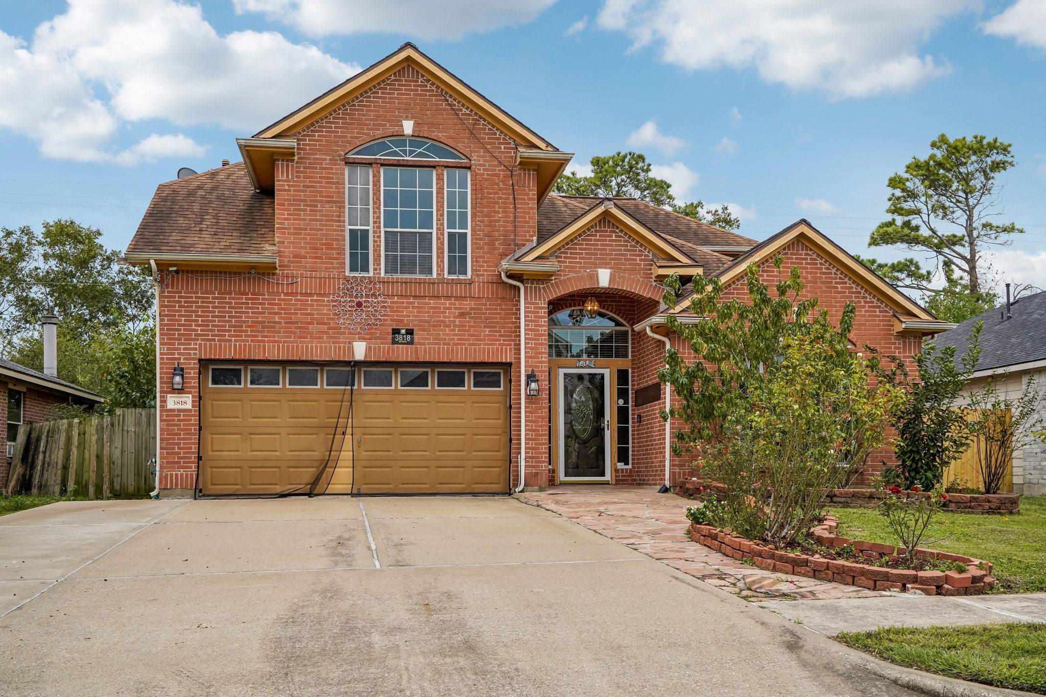 This photo features a two-story brick home with a double garage and an inviting front entrance. The property includes a spacious driveway, landscaped front yard with shrubs, and a welcoming pathway. The large windows provide ample natural light, and the architectural design adds to its curb appeal.