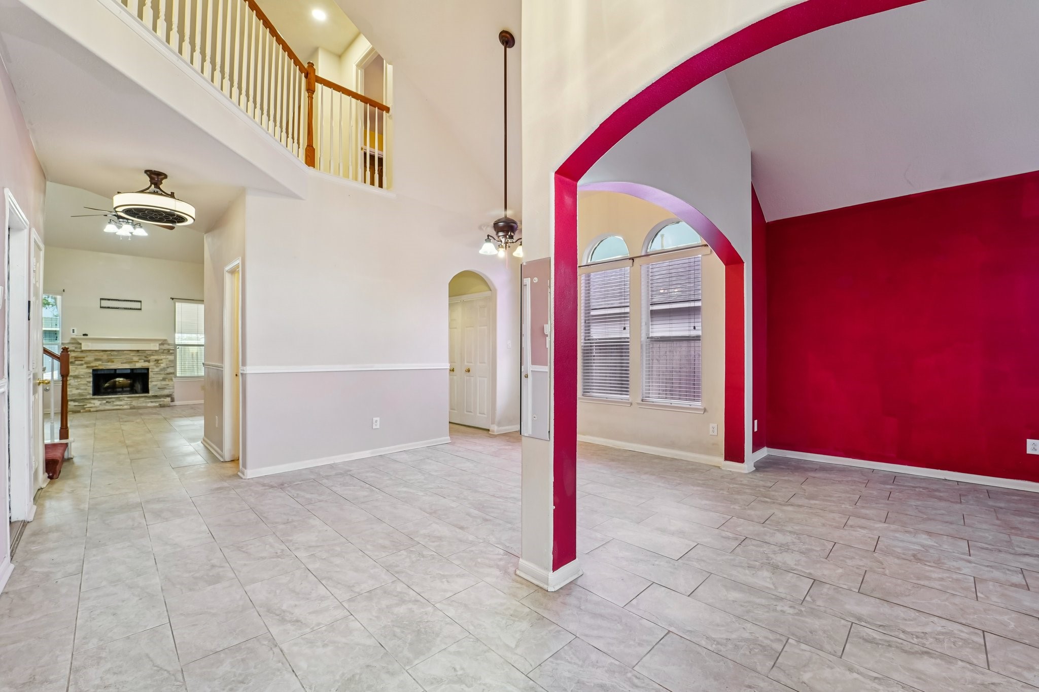 3818 Ridge Canyon Road Baytown, TX 77521 - Photo 13 of 42 This home features a spacious, open-concept living area with high ceilings and a vibrant red accent wall. The tile flooring extends throughout, and large windows offer plenty of natural light. A modern light fixture and a view of an upstairs railing add elegance, while an adjacent room with a fireplace creates a cozy atmosphere.