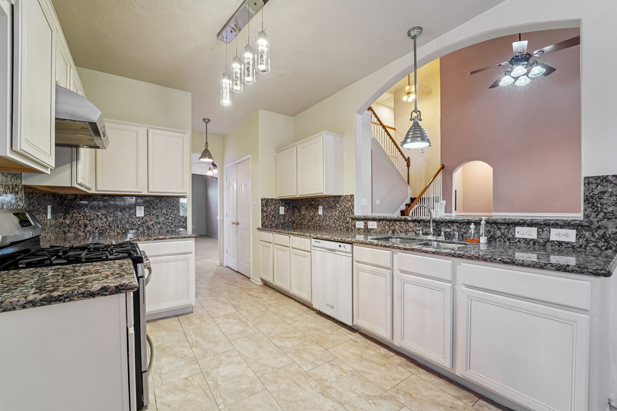 3818 Ridge Canyon Road Baytown, TX 77521 - Photo 17 of 42 This kitchen features elegant granite countertops, ample white cabinetry, and modern stainless steel appliances. It includes stylish pendant lighting and a view of the staircase through a large interior window, adding a spacious and connected feel.