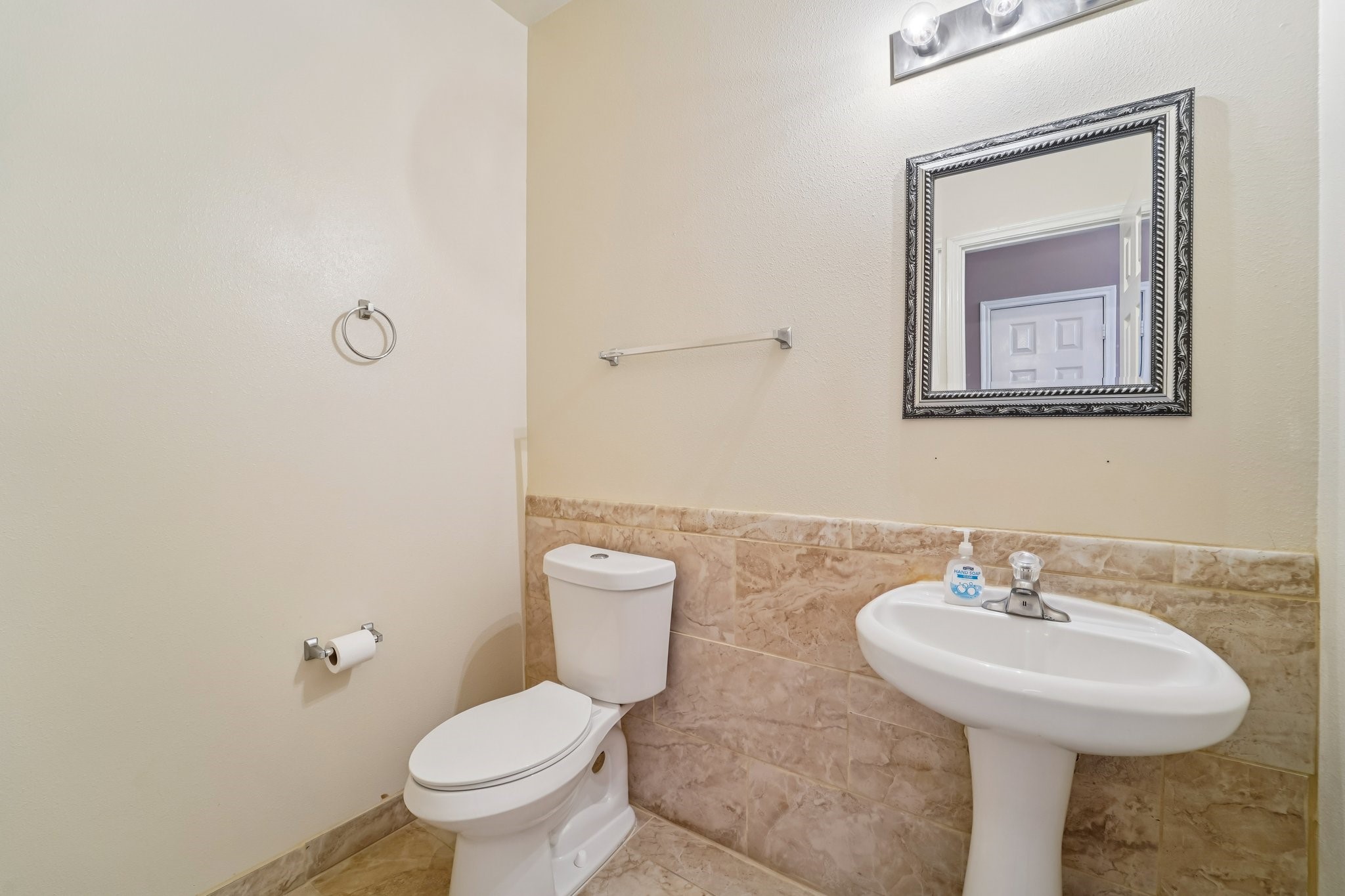 3818 Ridge Canyon Road Baytown, TX 77521 - Photo 18 of 42 This bathroom features a simple design with a pedestal sink and toilet. It has neutral tile halfway up the walls, a framed mirror, and a modern light fixture above.