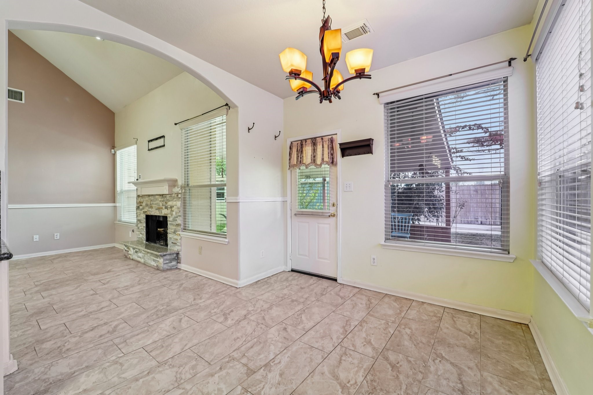 3818 Ridge Canyon Road Baytown, TX 77521 - Photo 19 of 42 This bright, airy room features a high ceiling, elegant chandelier, and large windows for ample natural light. It includes a cozy fireplace with a stone surround and stylish tile flooring, creating a welcoming atmosphere.
