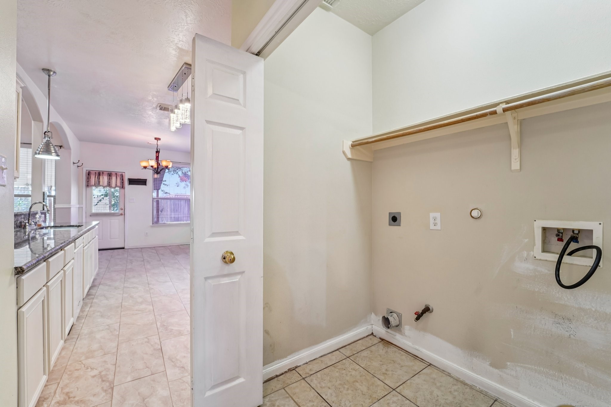 3818 Ridge Canyon Road Baytown, TX 77521 - Photo 21 of 42 This photo shows a utility area with hookups for a washer and dryer, adjacent to a bright kitchen featuring granite countertops and white cabinetry. The space opens into a dining area with tile flooring and a large window for natural light.