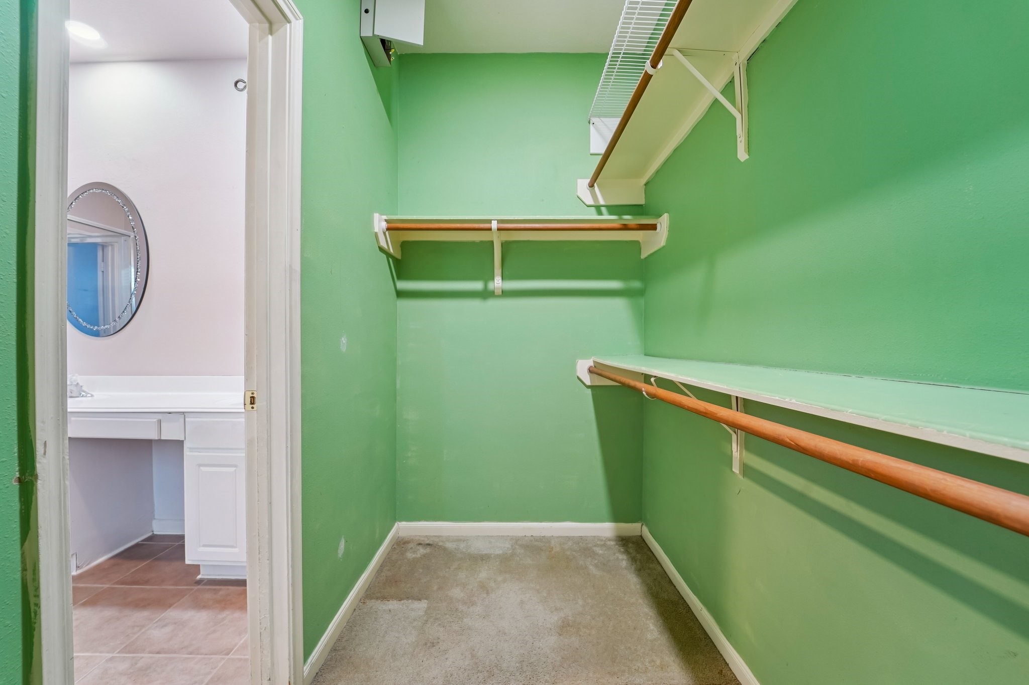 3818 Ridge Canyon Road Baytown, TX 77521 - Photo 22 of 42 This photo shows a walk-in closet with green walls, featuring wooden and wire shelving for ample storage. It connects to a bathroom with a vanity and mirror visible in the background.