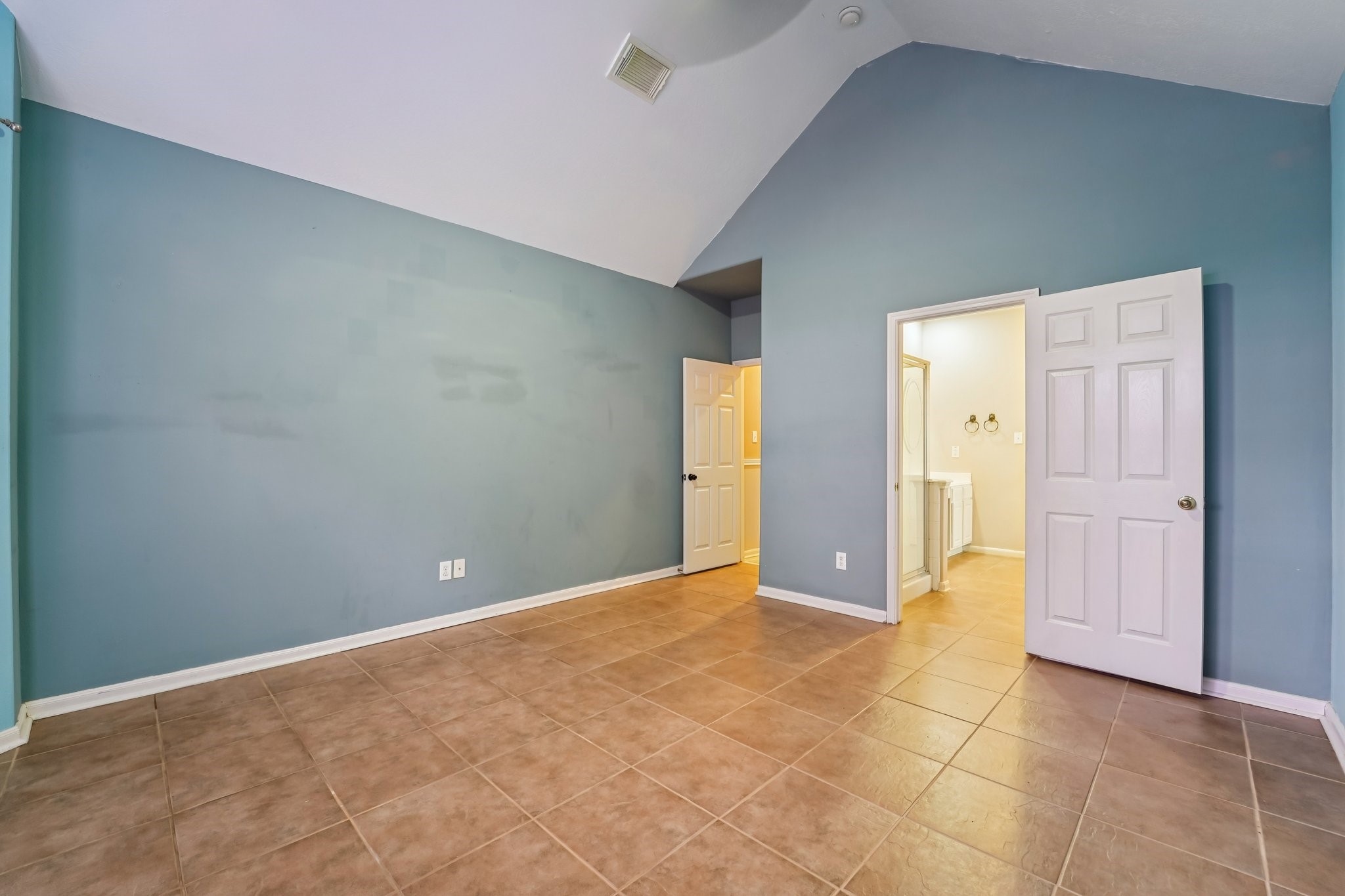 3818 Ridge Canyon Road Baytown, TX 77521 - Photo 26 of 42 This photo showcases a spacious room with high ceilings and tiled floors. It features soft blue walls and two doorways, one leading to a bathroom, suggesting it's a master bedroom.