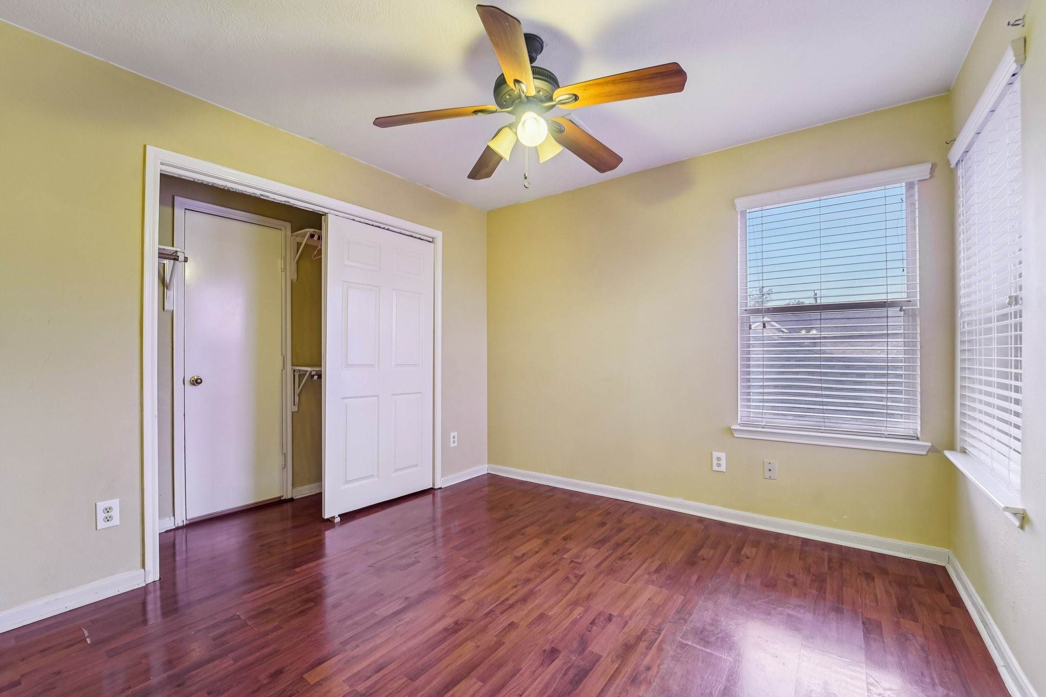 3818 Ridge Canyon Road Baytown, TX 77521 - Photo 31 of 42 Bright bedroom with warm yellow walls and wood flooring, featuring a ceiling fan and natural light from two windows. Includes a closet with sliding doors.