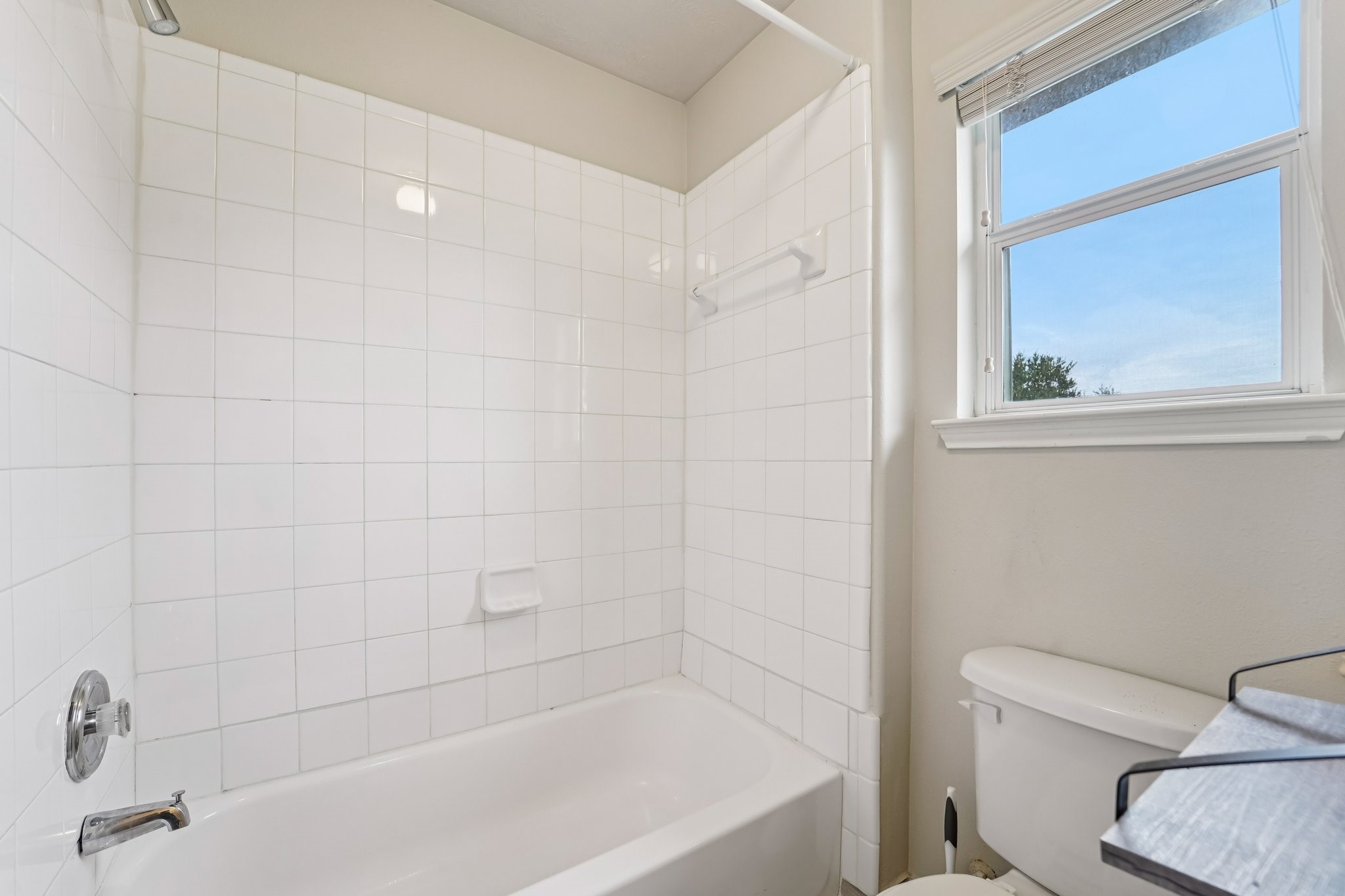 3818 Ridge Canyon Road Baytown, TX 77521 - Photo 36 of 42 This bathroom features a clean design with a white tiled shower and bathtub, ample natural light from a window, and a modern toilet. Perfect for a fresh and bright space.