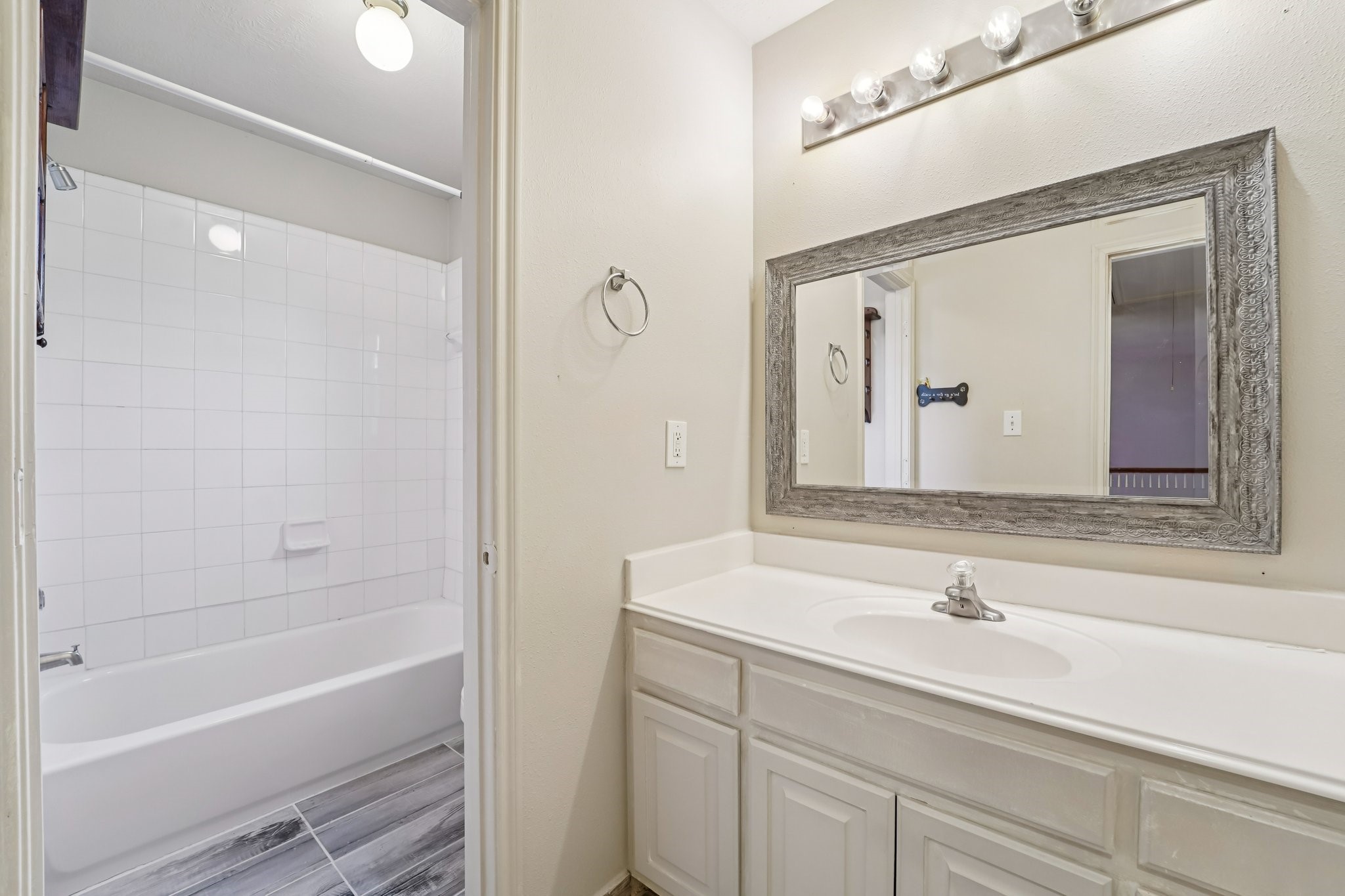 3818 Ridge Canyon Road Baytown, TX 77521 - Photo 37 of 42 This bathroom features a clean, modern design with a large framed mirror above a single-sink vanity. It includes a bathtub with tiled walls and a sleek, tiled floor, offering a bright and functional space.