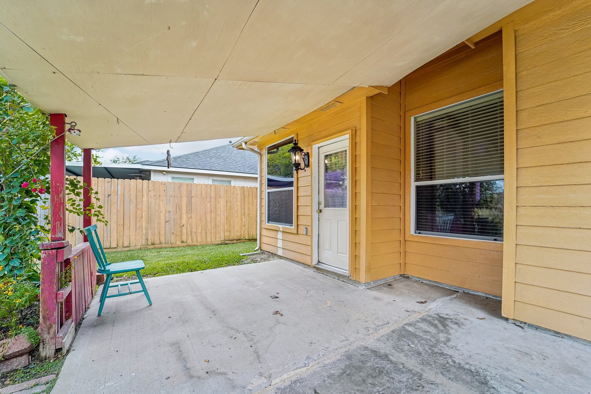3818 Ridge Canyon Road Baytown, TX 77521 - Photo 38 of 42 This photo showcases a cozy patio with a covered area, featuring a single chair and a charming outdoor light fixture. The space is adjacent to a well-maintained lawn, enclosed by a wooden fence, perfect for relaxation and privacy.