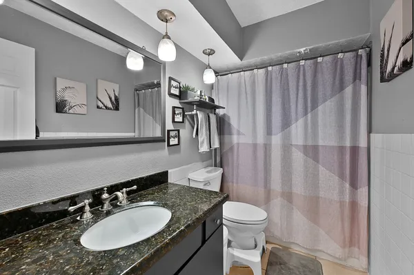 a bathroom with a granite countertop sink a toilet a mirror and shower curtain