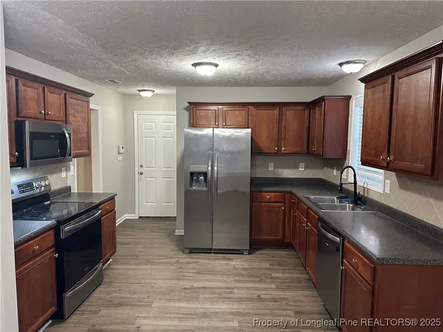 a kitchen with stainless steel appliances granite countertop a refrigerator a sink a stove a oven with wooden cabinets and floor