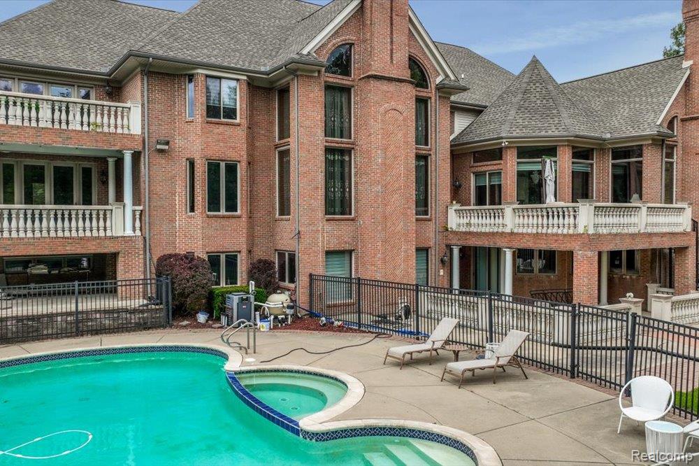 3543 Cedar Brook Drive Rochester, MI 48309 - Photo 93 of 99 Brick exterior with multiple balconies featuring balustrade railings, large windows, and an outdoor pool with an integrated spa
