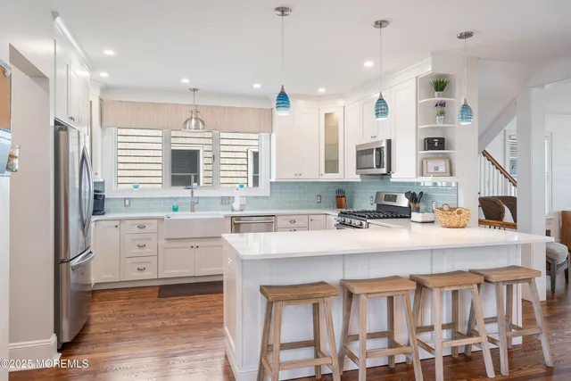 a kitchen with stainless steel appliances granite countertop a stove top oven a sink dishwasher and white cabinets with wooden floor