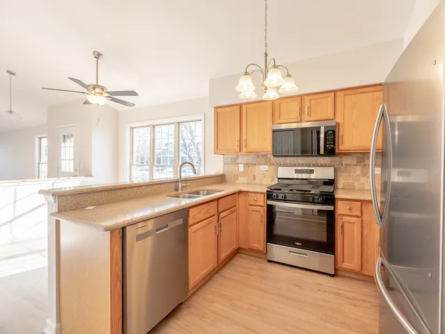 a kitchen with stainless steel appliances granite countertop a sink a stove a refrigerator cabinets and a dining table with wooden floor